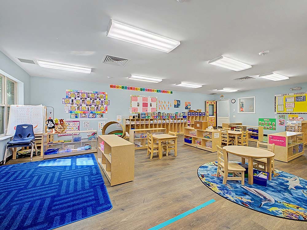 Classroom with small tables and chairs, shelves with toys, and colorful artwork on the walls