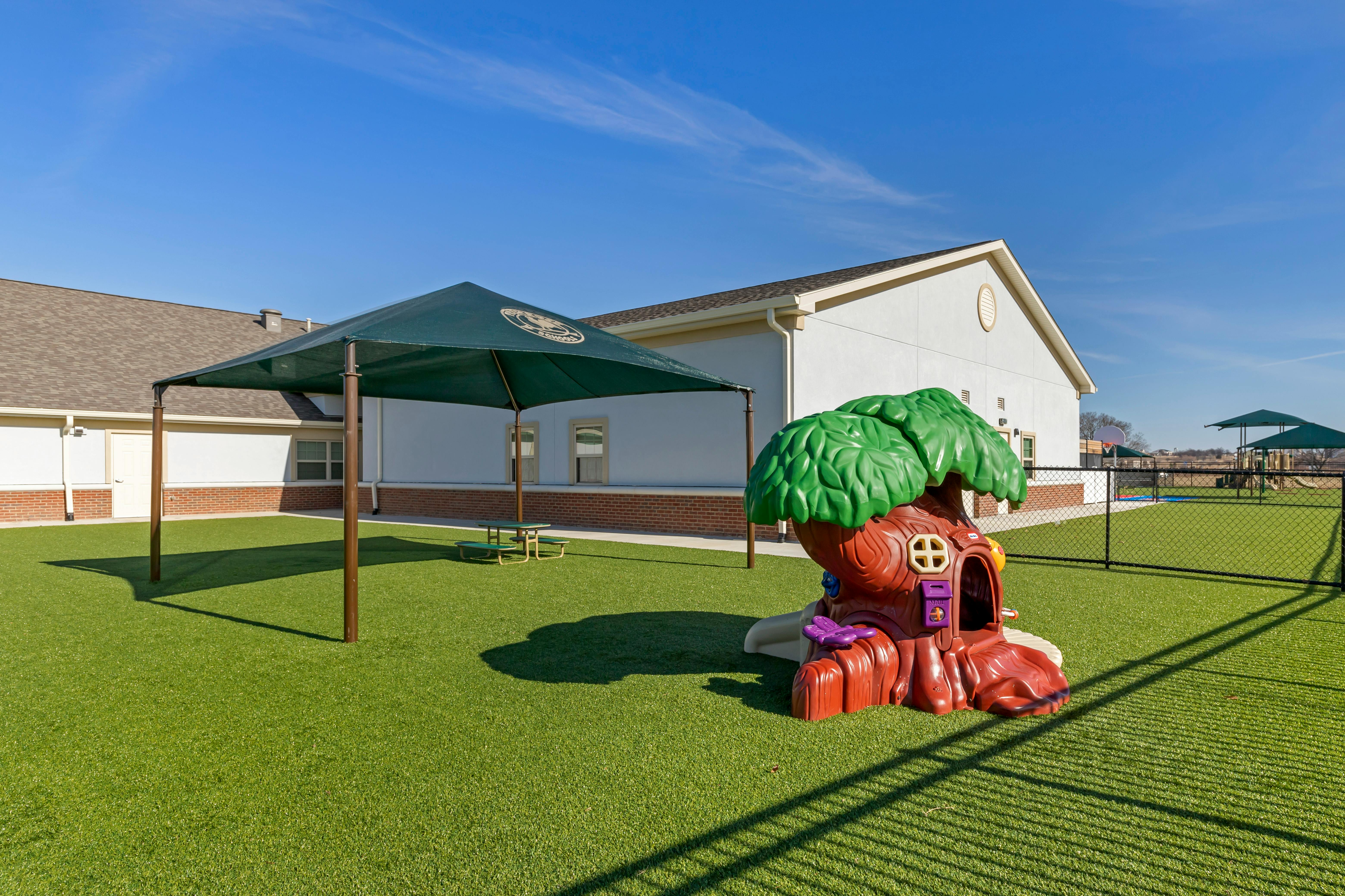 Playground area with a sunshade, picnic table, and treehouse play structure