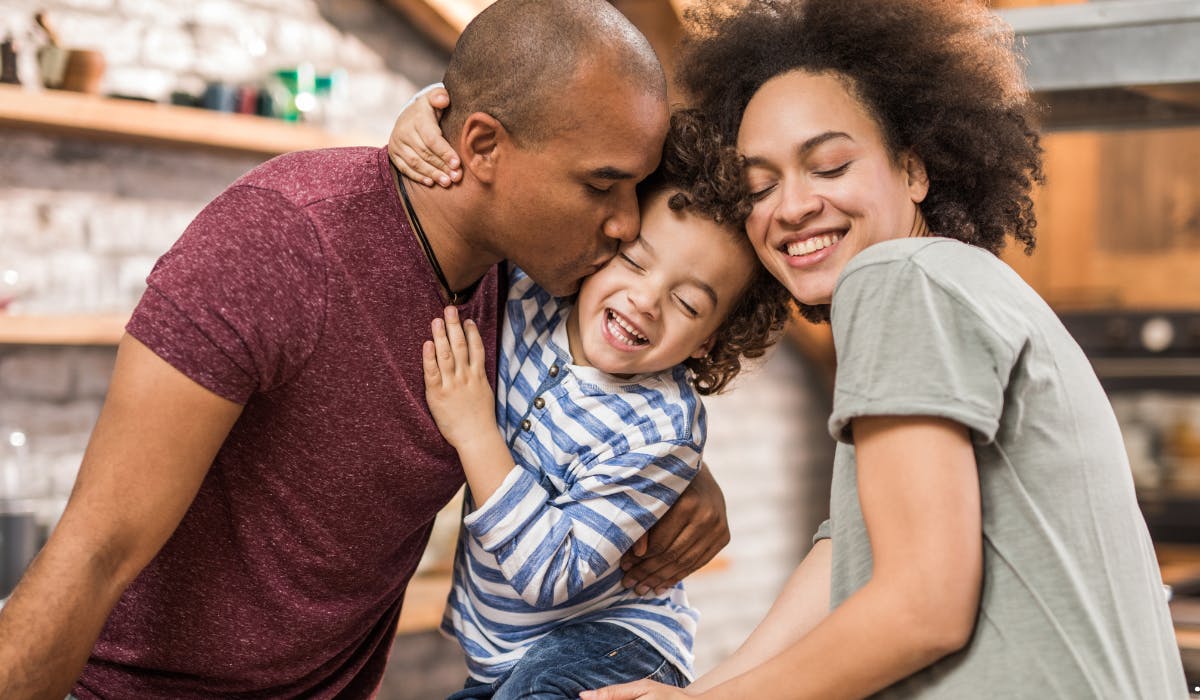 Adult person kissing a child on the head, another adult person smiling