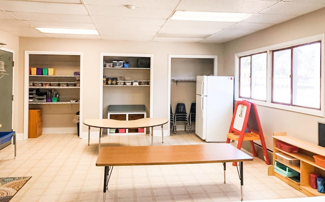 Empty classroom with tables, shelves, and a refrigerator