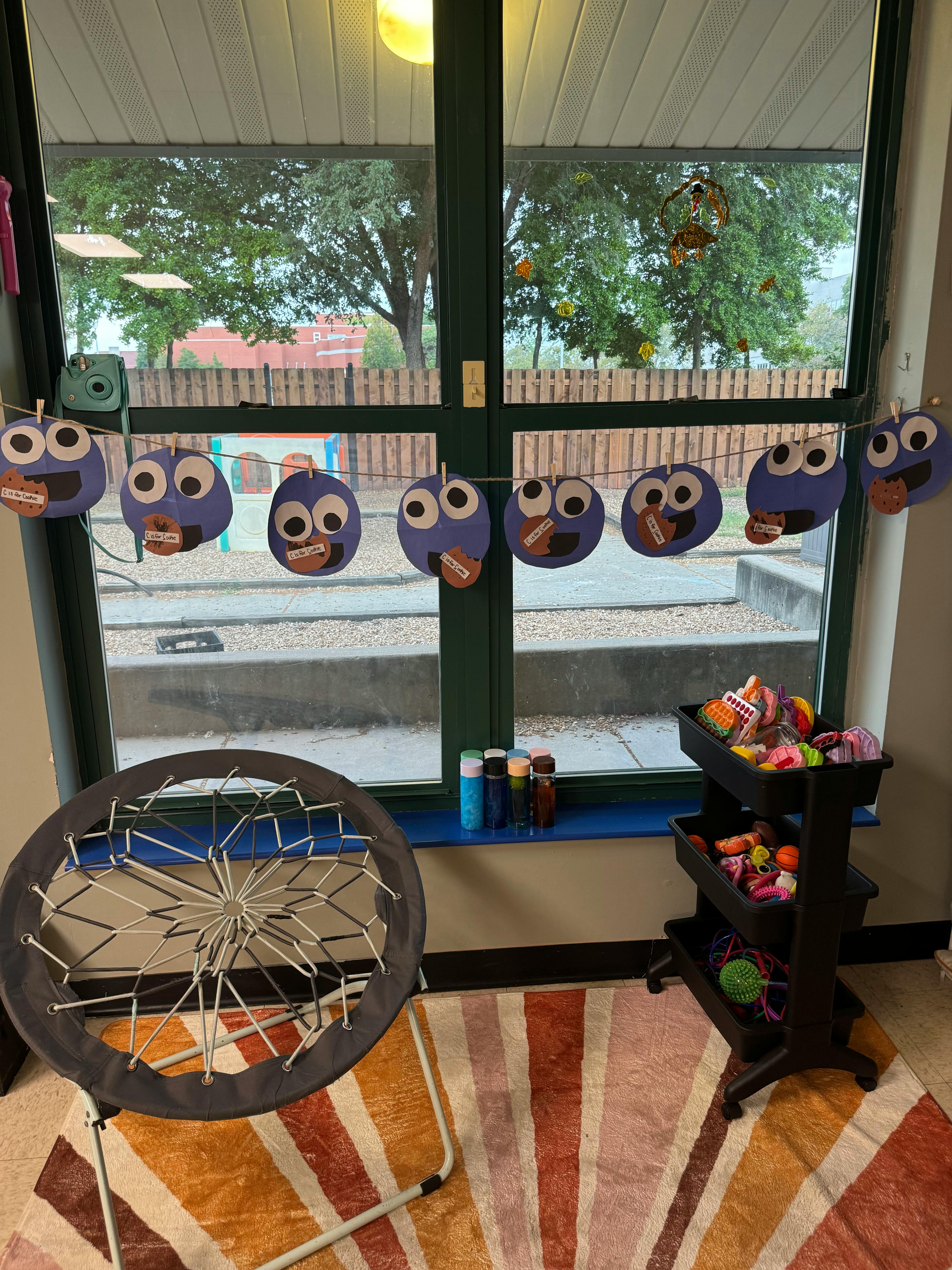 Owl decorations hanging in a window above a chair and toy organizer