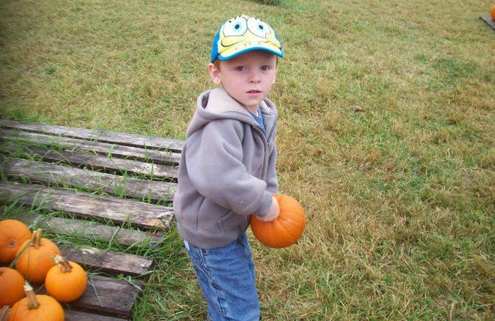 Child holding a small pumpkin in a grassy field