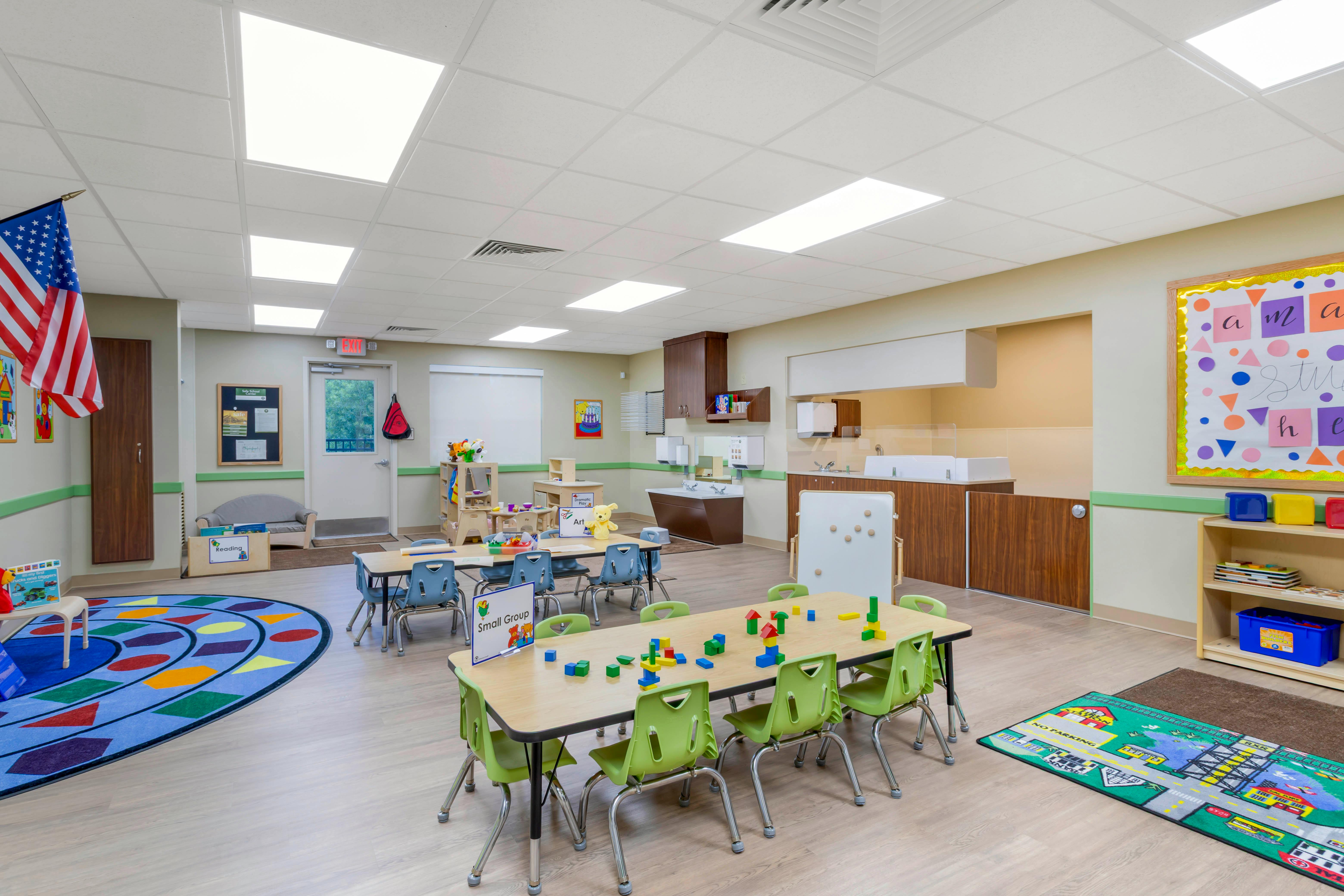 Classroom with small tables and chairs, a play rug, and activity areas