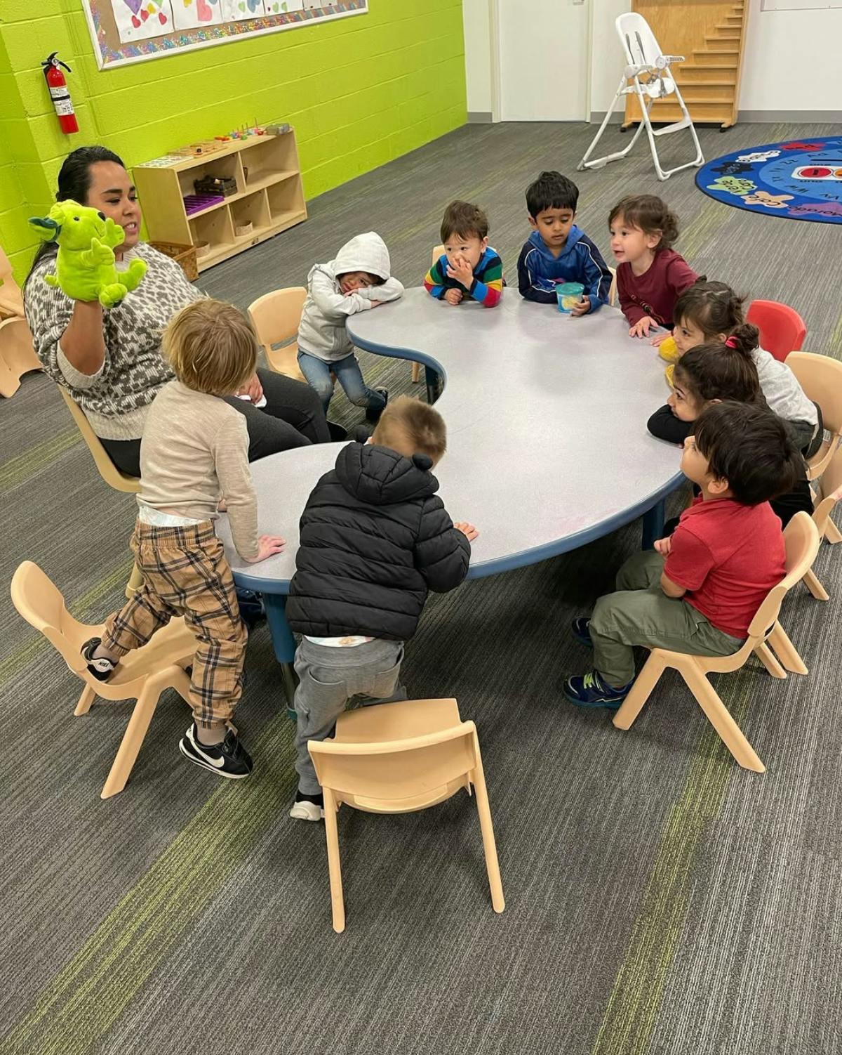Adult holding a puppet for children gathered around a table in a classroom