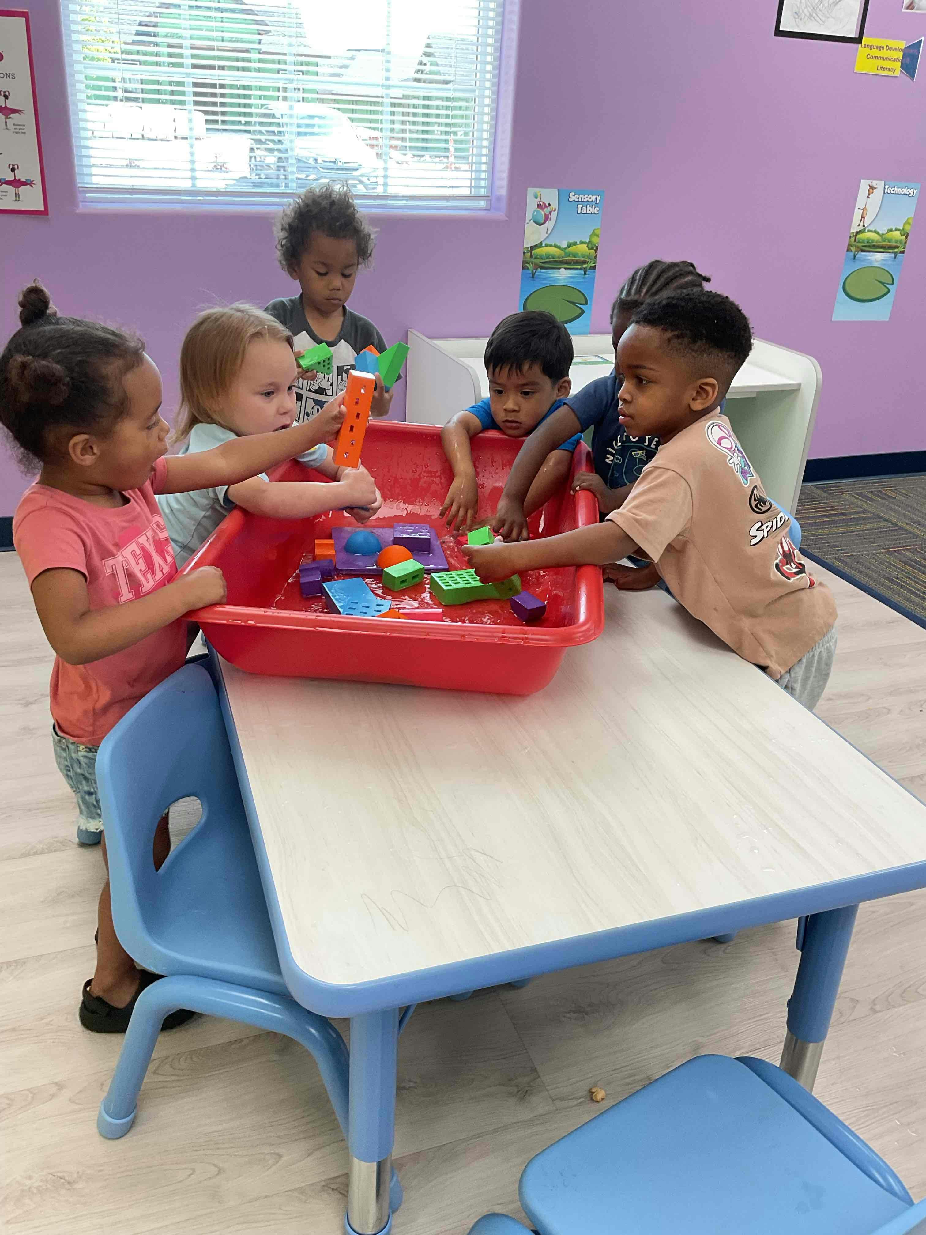 Children playing with toys in a red bin on a table in a classroom