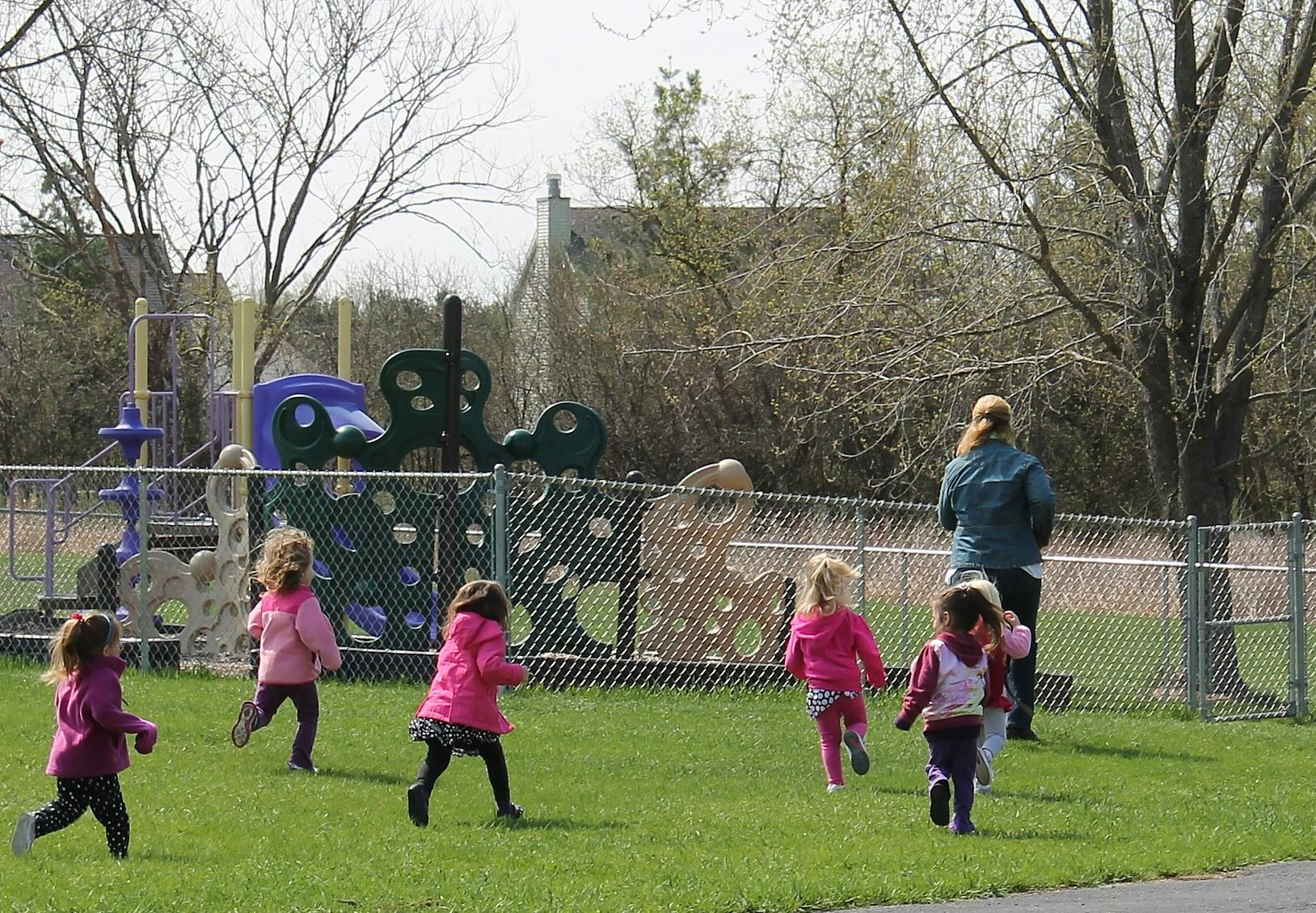 Children running on grass with a person on a playground