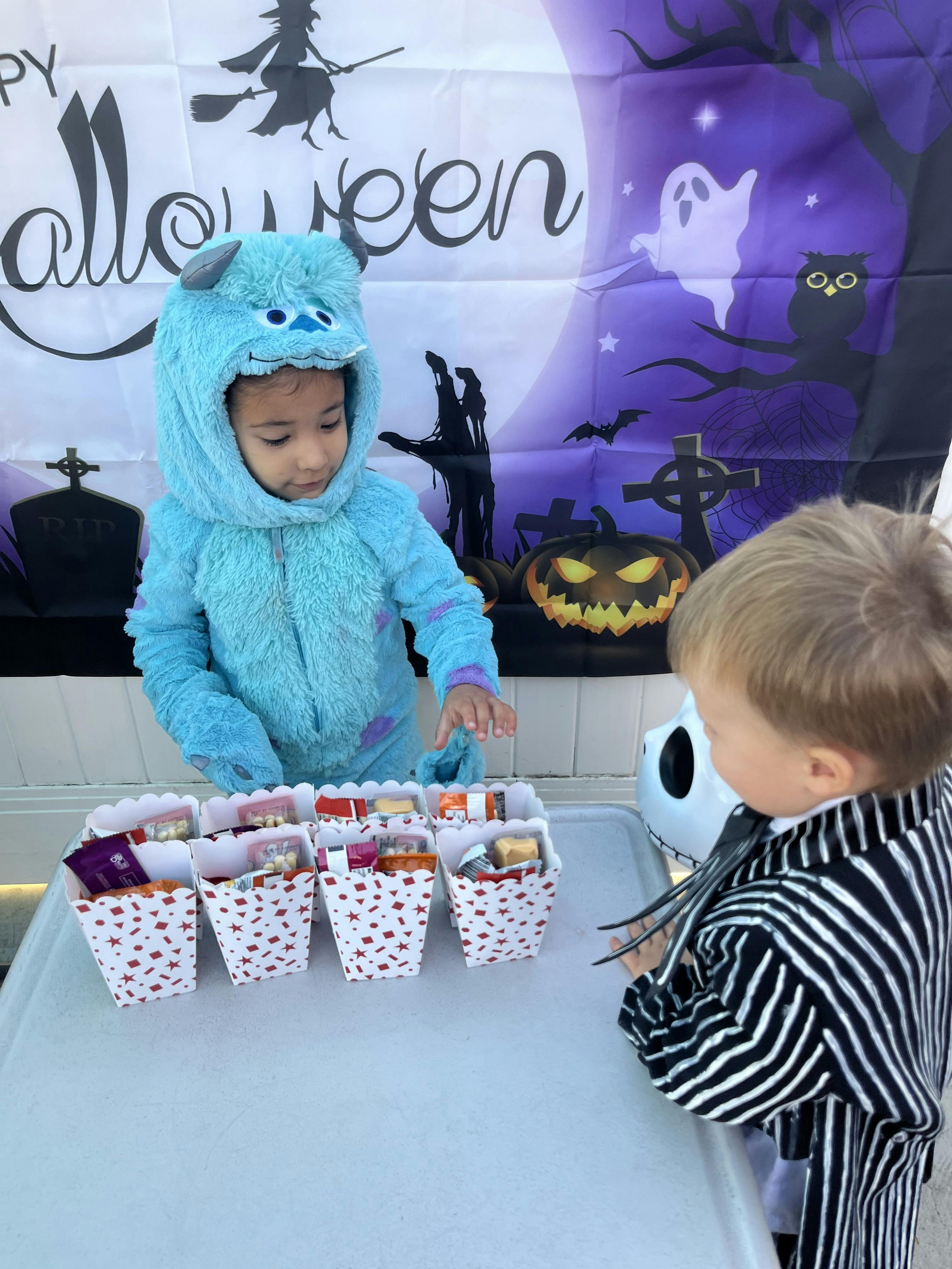 Child in blue monster costume offering treats to another child