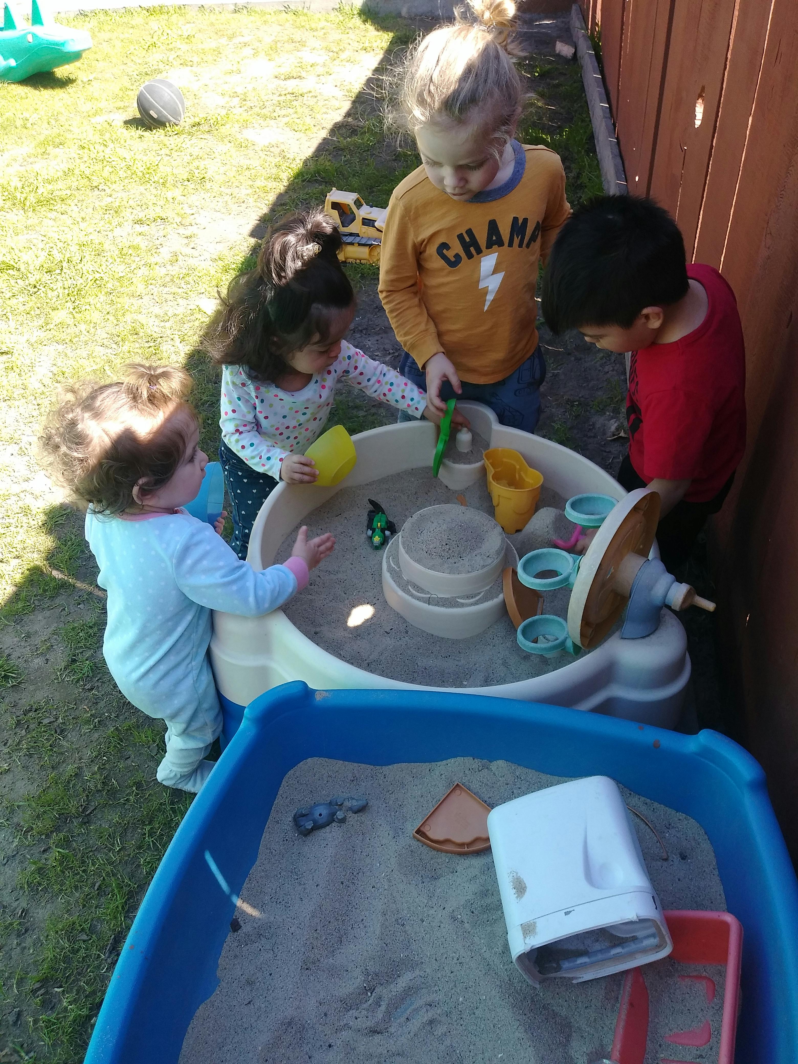 Four children playing with a sand and water table outdoors