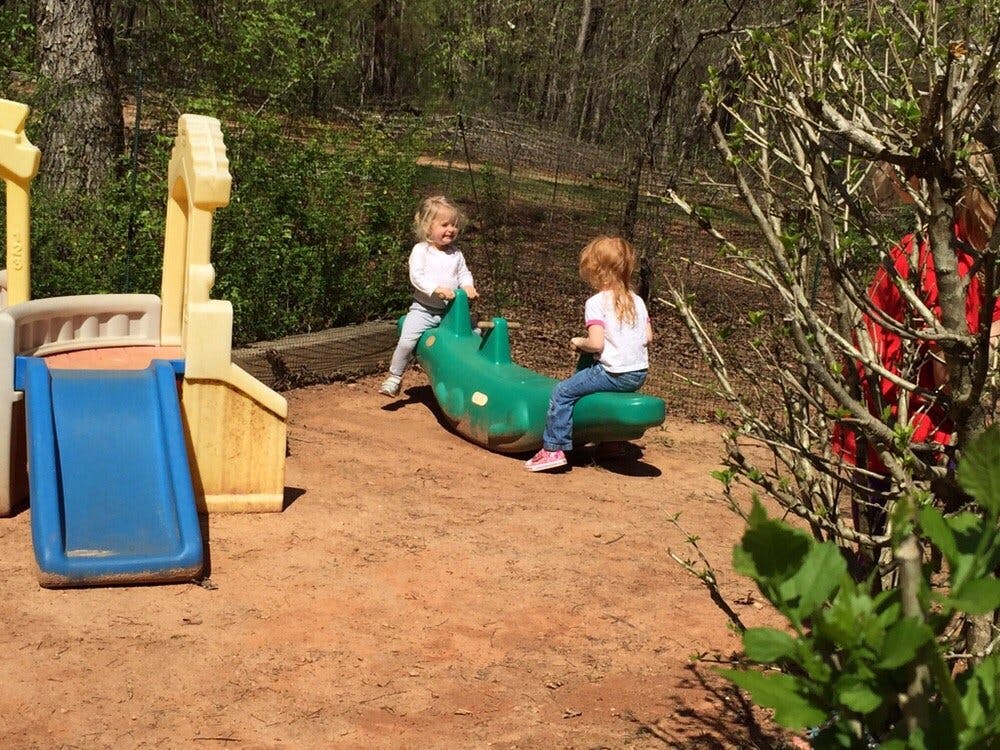 Two children playing on a green seesaw in a playground