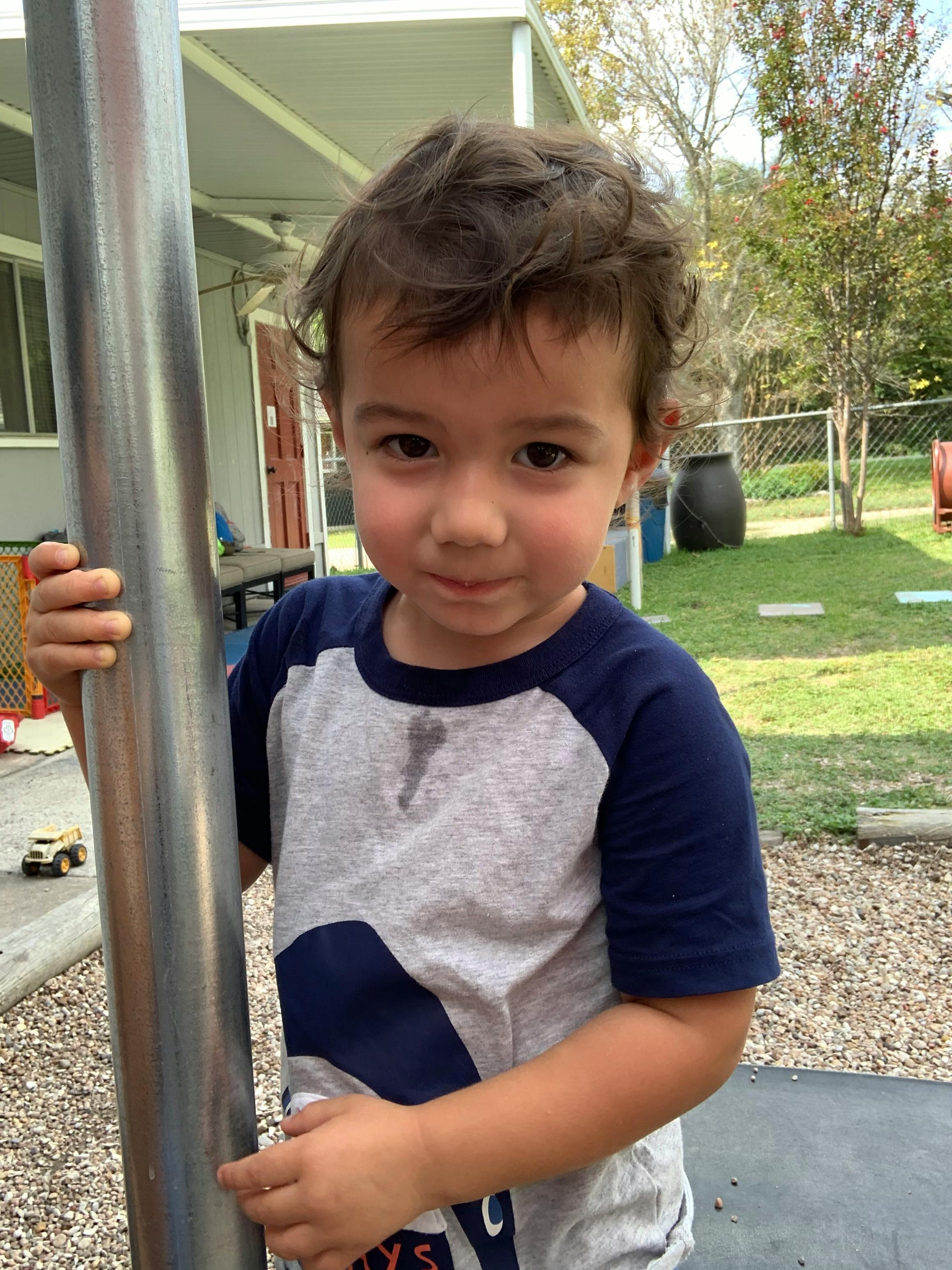 Child holding onto a metal pole outdoors