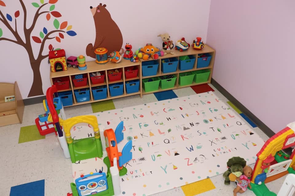Playroom with alphabet rug, toy shelf, and various toys