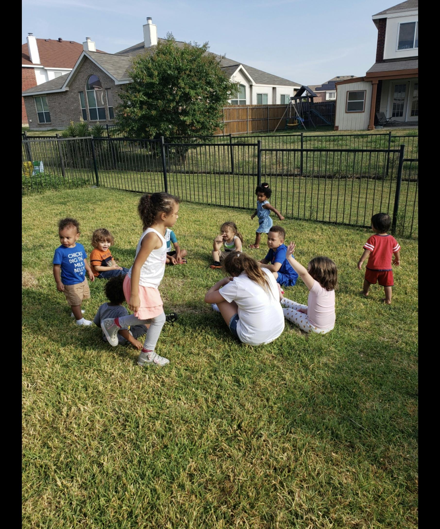 Children and adults sitting and standing in a grassy yard