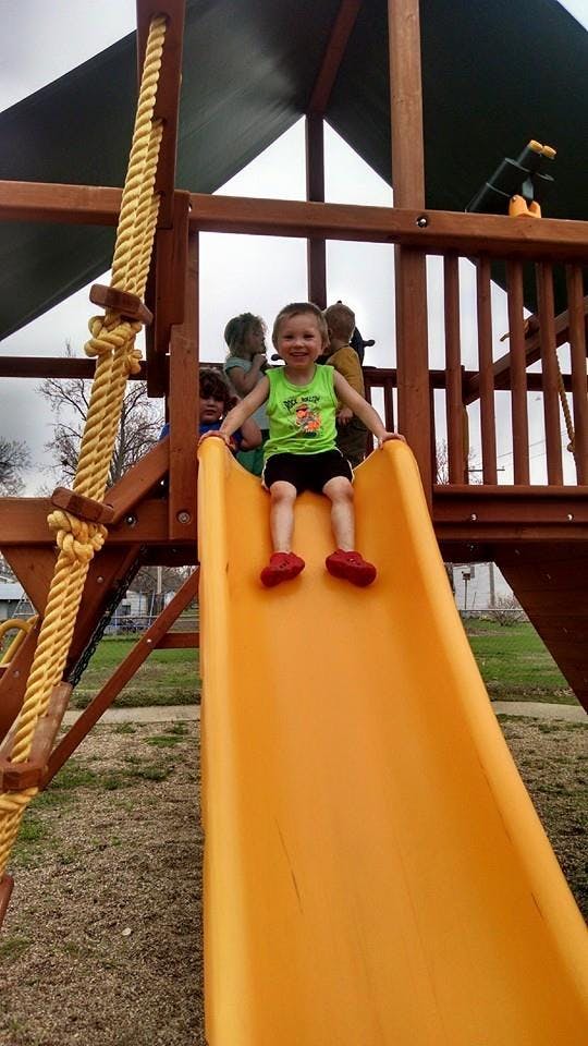 Child sitting at the top of a yellow slide on a playground