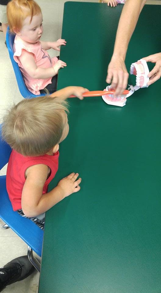 Child brushing a model of teeth with a toothbrush at a green table