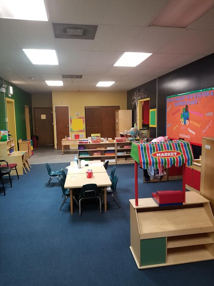Classroom with small tables and chairs, shelves, and a play market stand