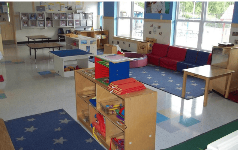 Empty classroom with colorful rugs, tables, shelves, and red and blue couches