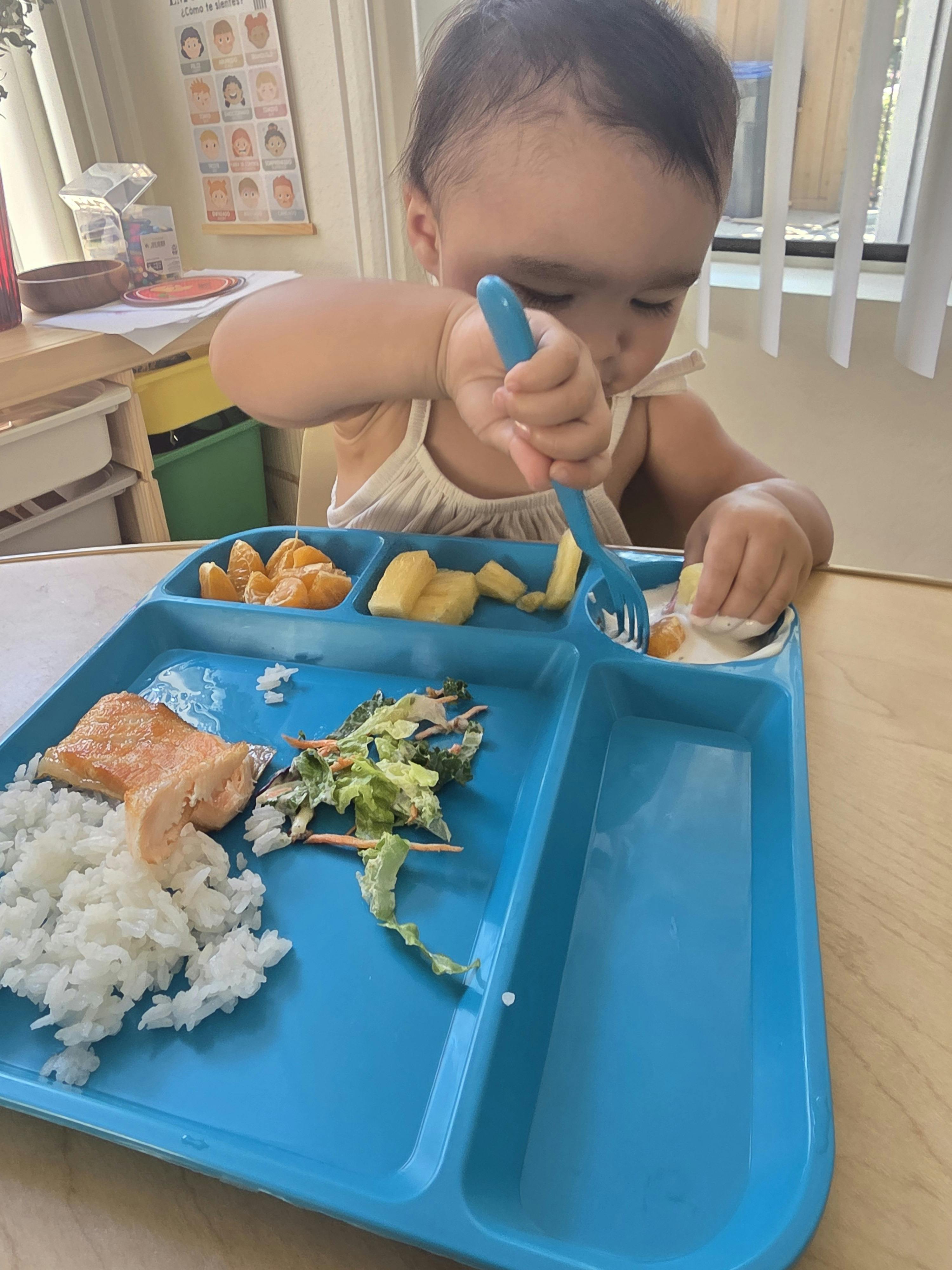 Child eating from a sectioned tray with a fork