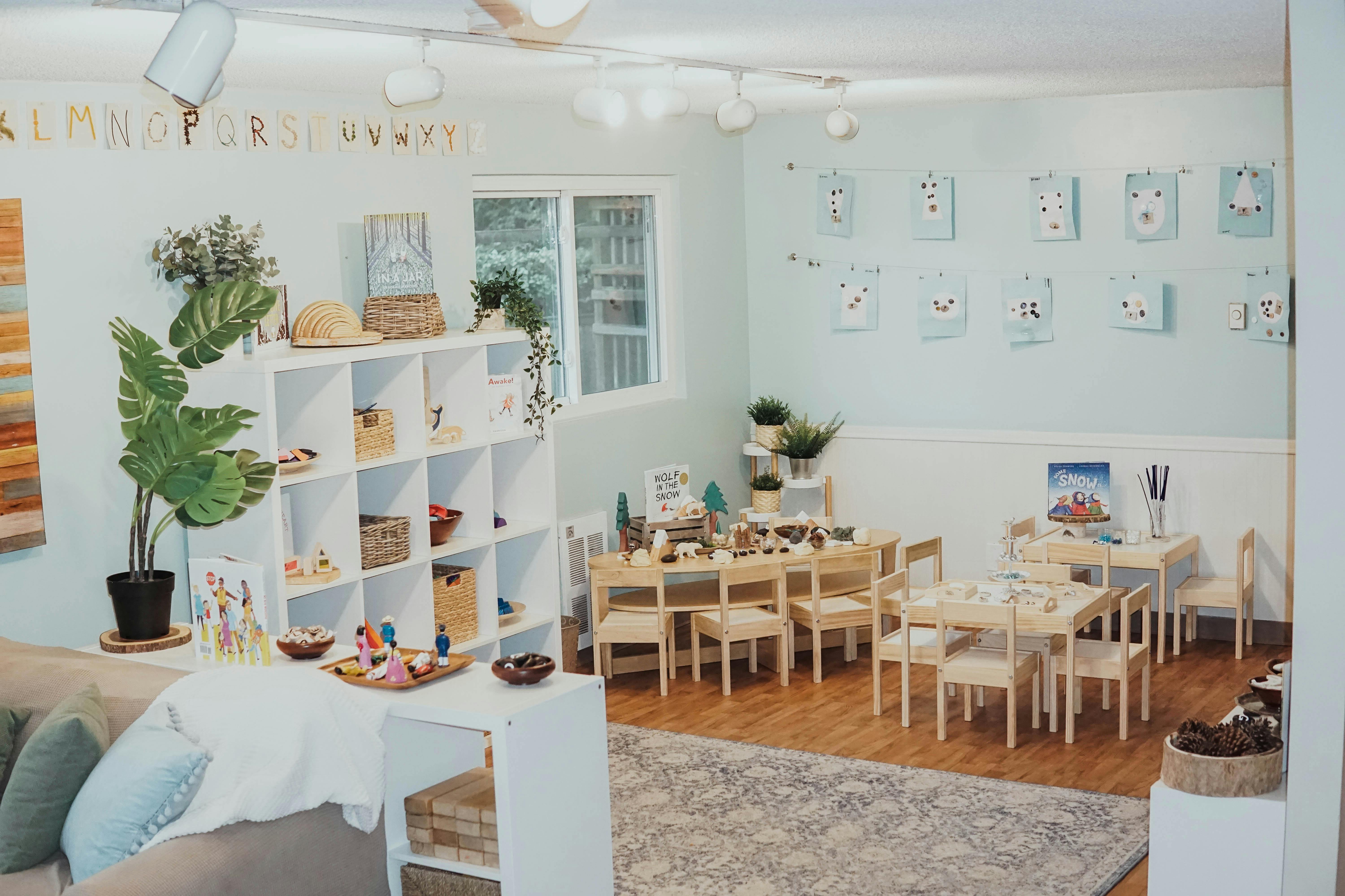 Classroom with small tables and chairs, a white cubby shelf, and light blue walls
