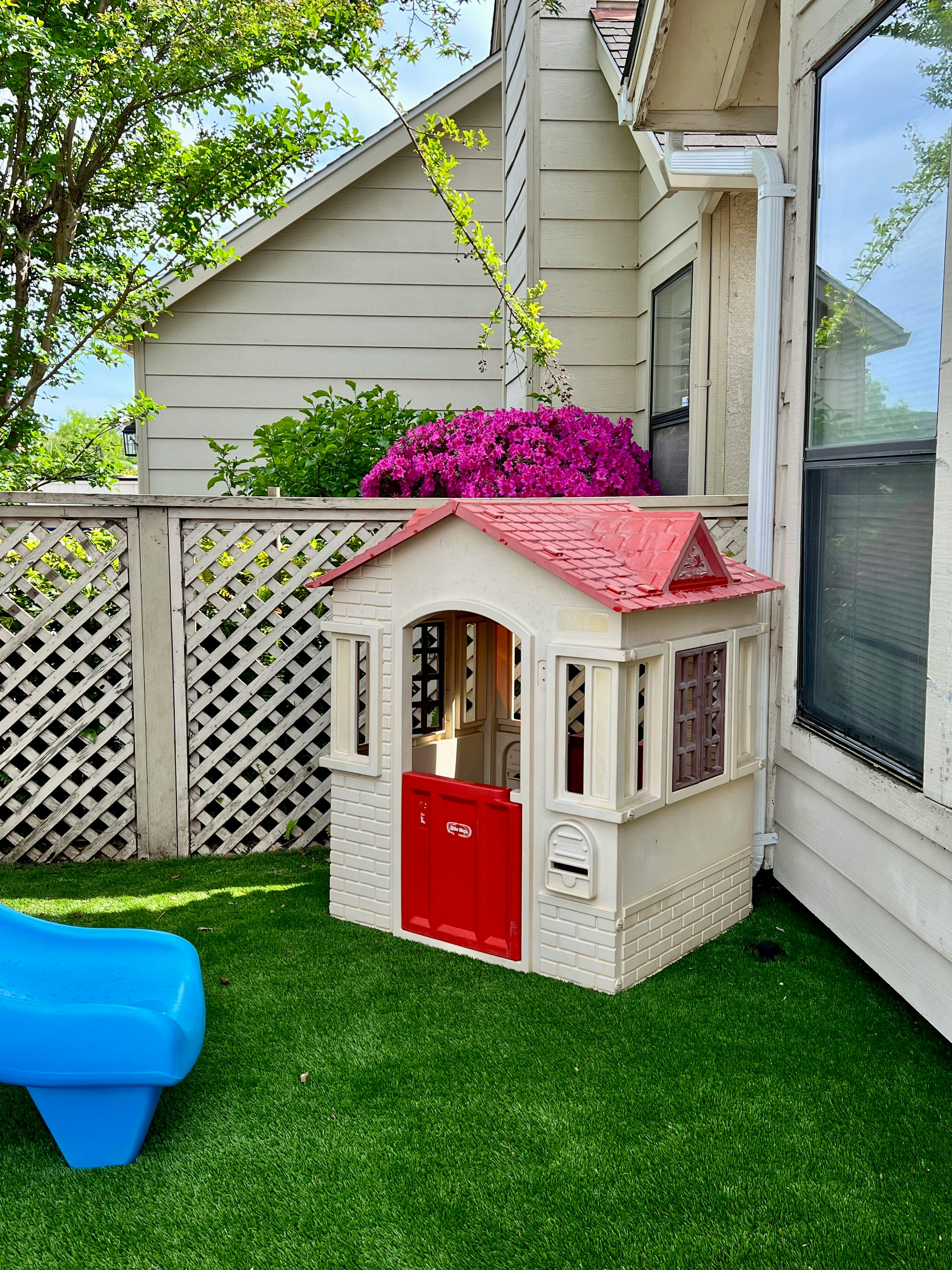 Child's playhouse with red roof and door next to a blue slide