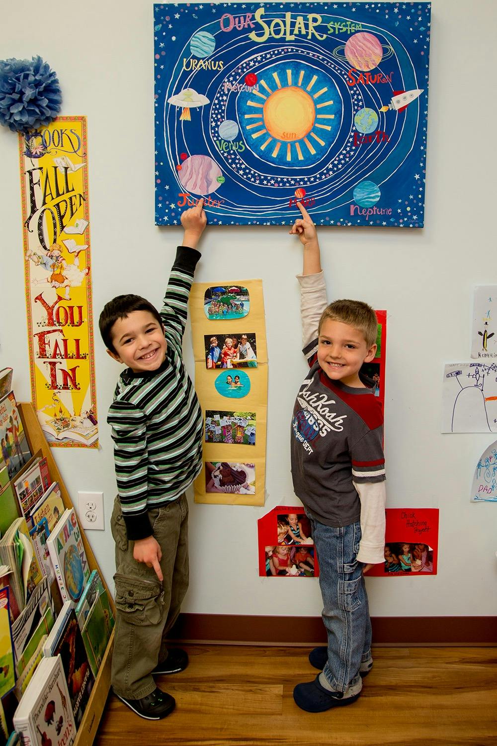 Two children pointing at a solar system poster on a wall in a classroom
