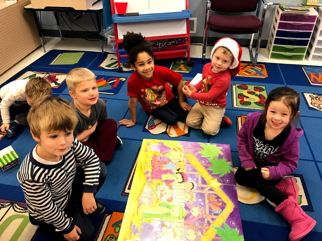 Children sitting on a blue mat with a large colorful board game