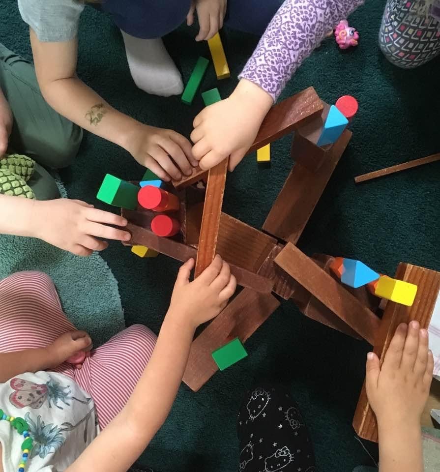 Children playing with wooden blocks and colorful shapes on a green surface