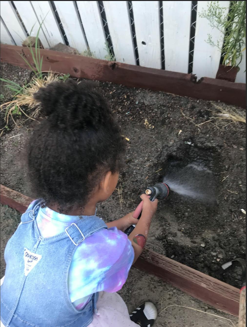 Child watering dirt with a hose