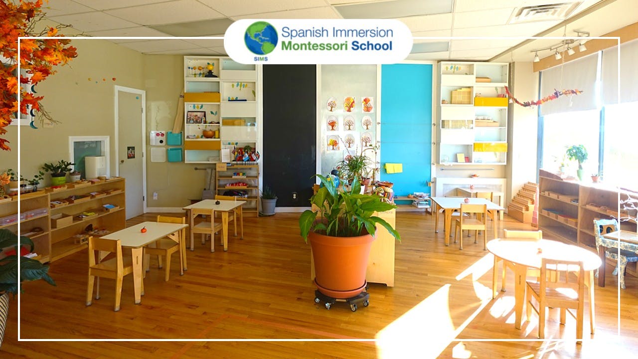 Classroom with small tables and chairs, shelves with learning materials