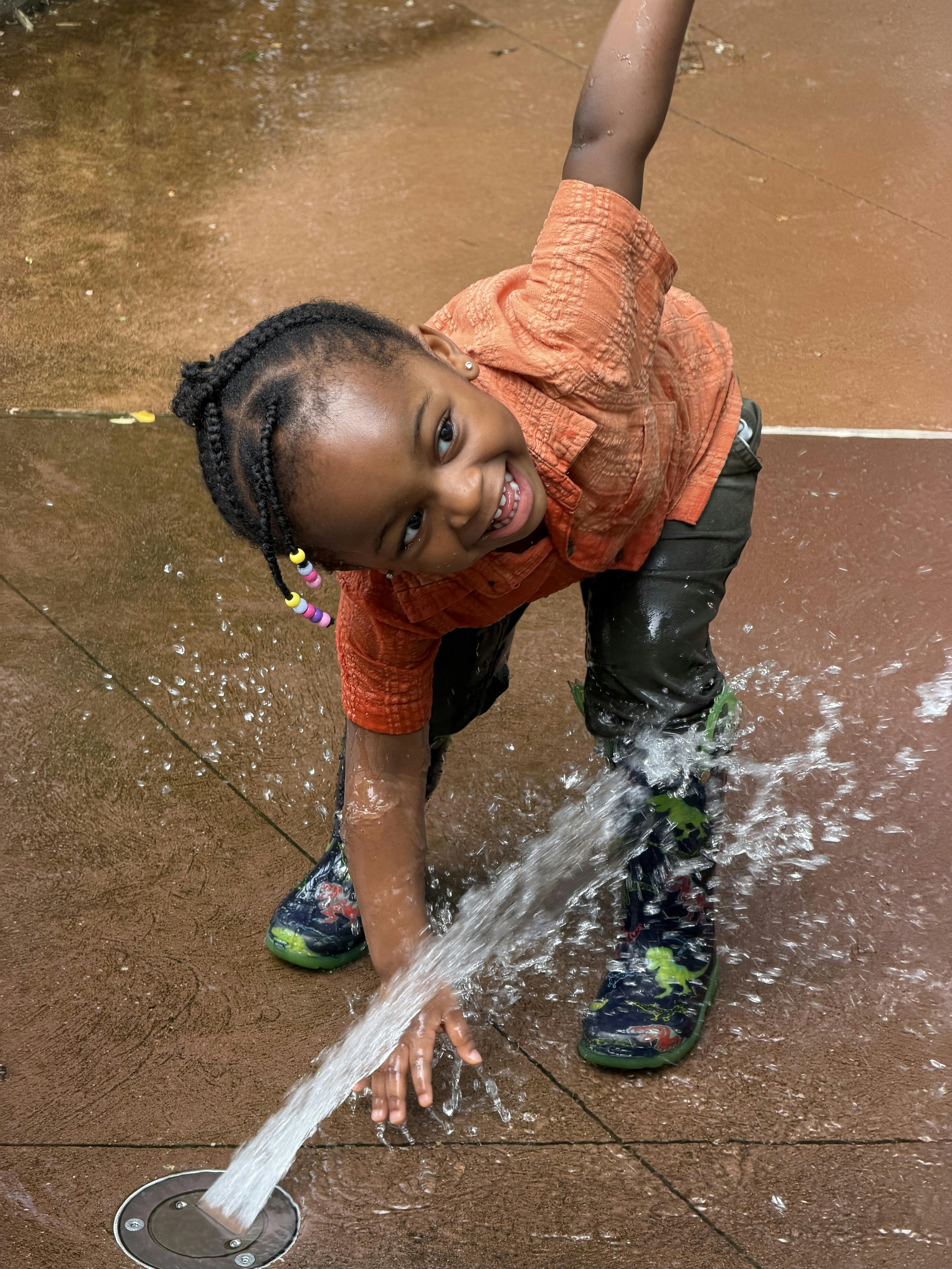 Child in boots playing with water spraying from the ground