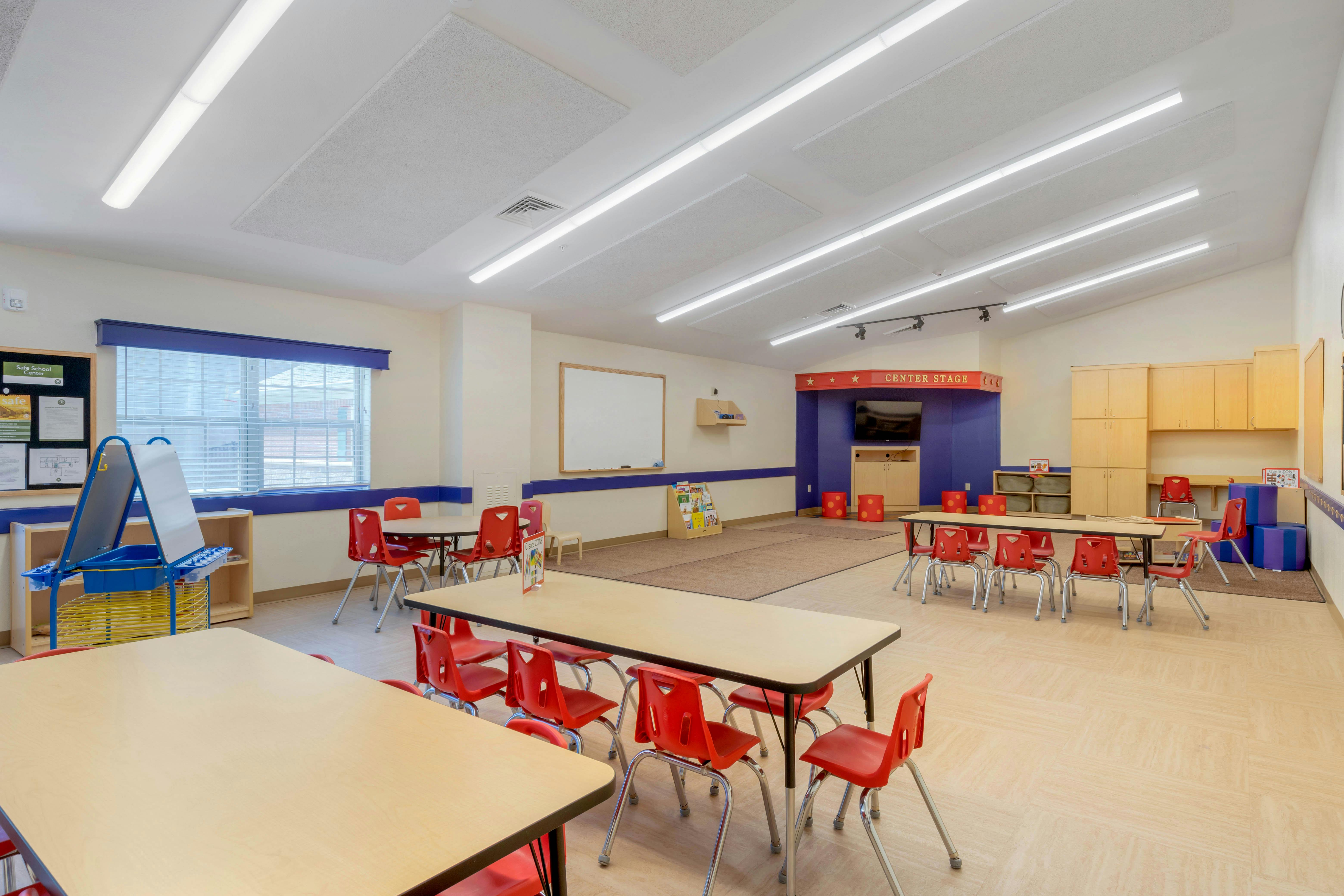 An empty classroom with small tables and red chairs, a whiteboard, and a "Center Stage" area