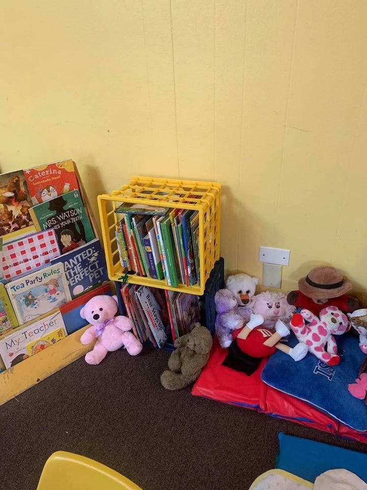 Books in a yellow crate and on shelves with stuffed animals on the floor