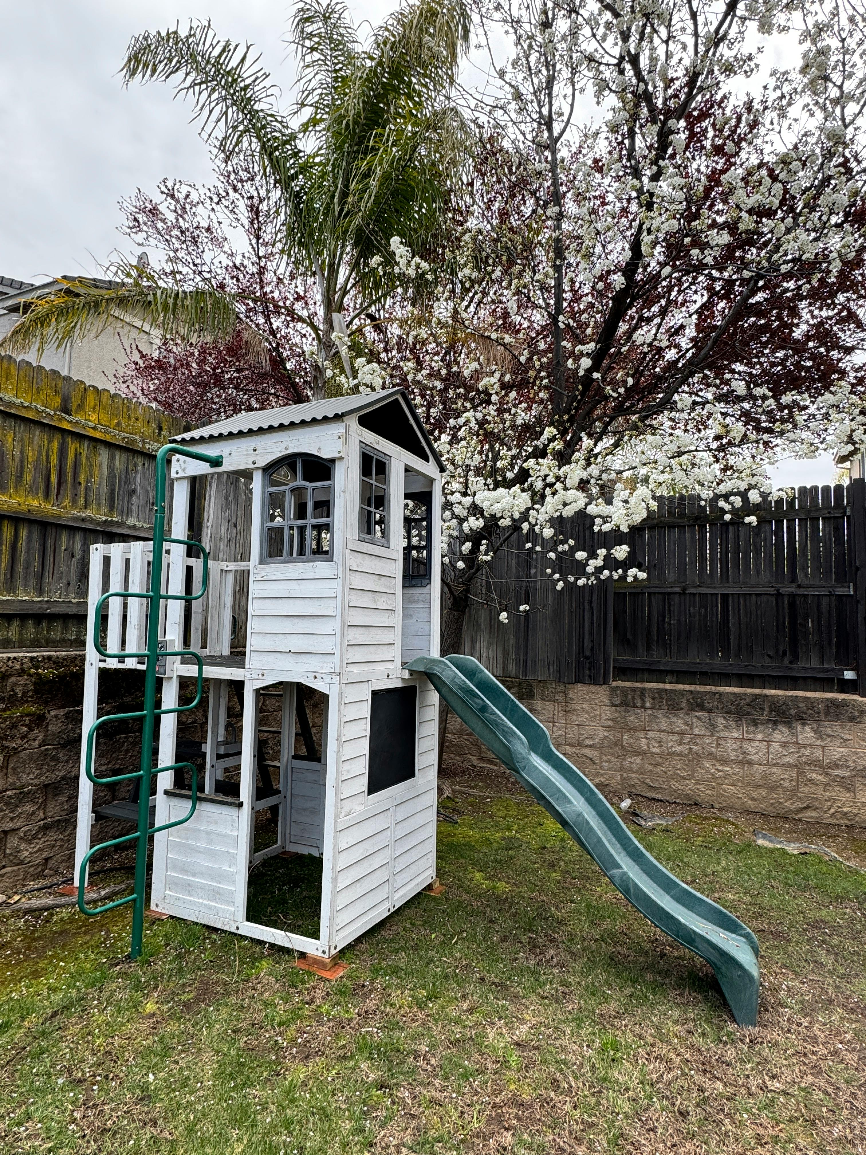 White wooden playhouse with a green slide in a grassy yard