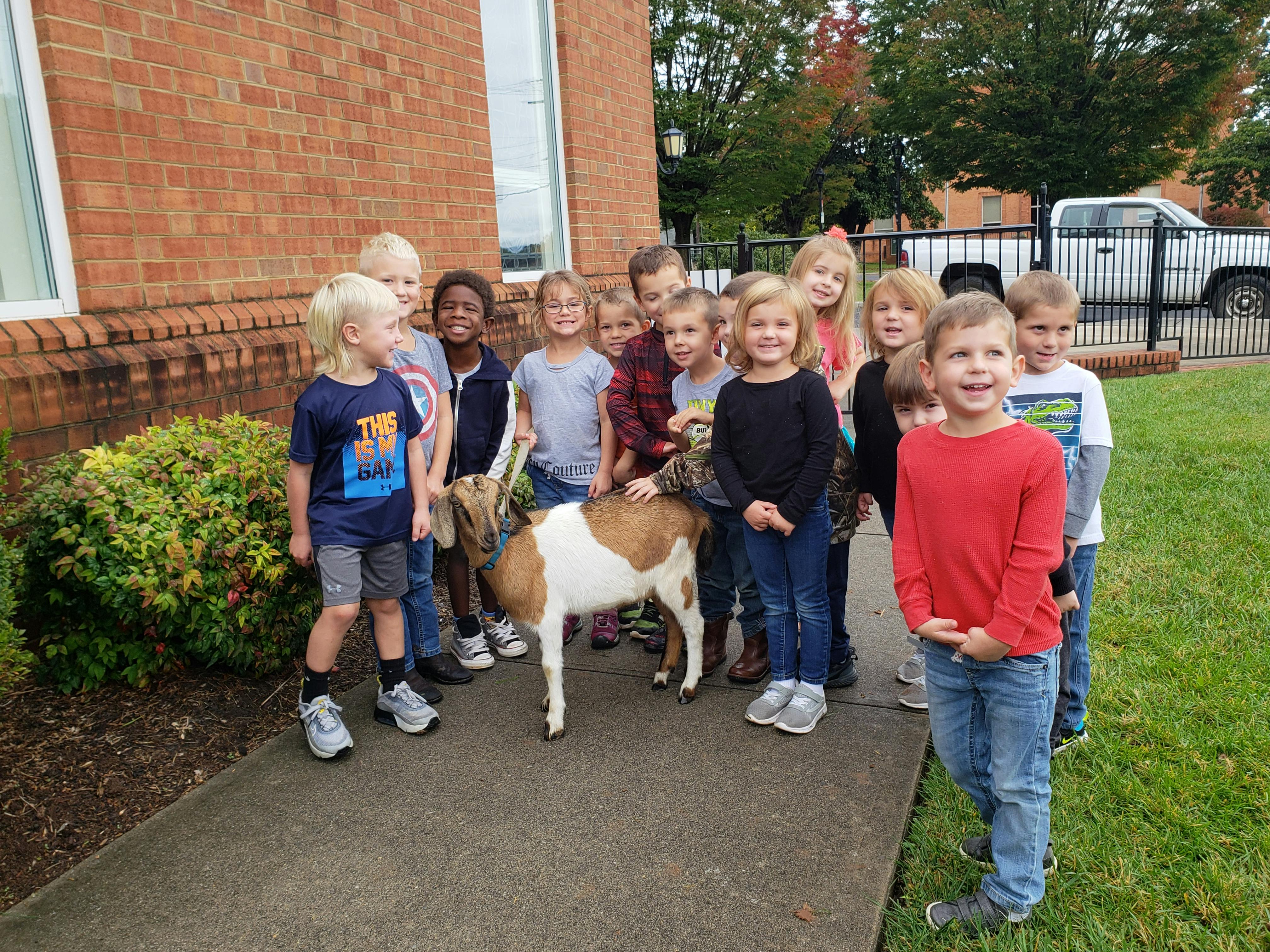 Group of children standing with a goat on a sidewalk