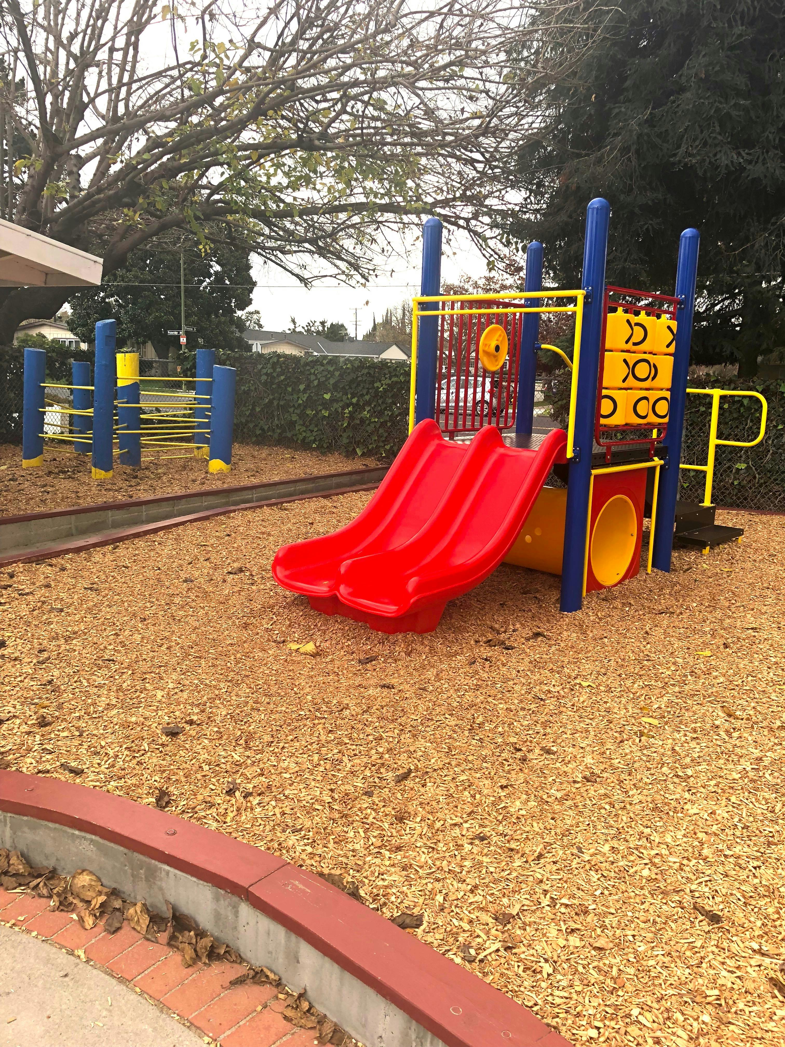 Red slides on a playground structure with wood chips on the ground