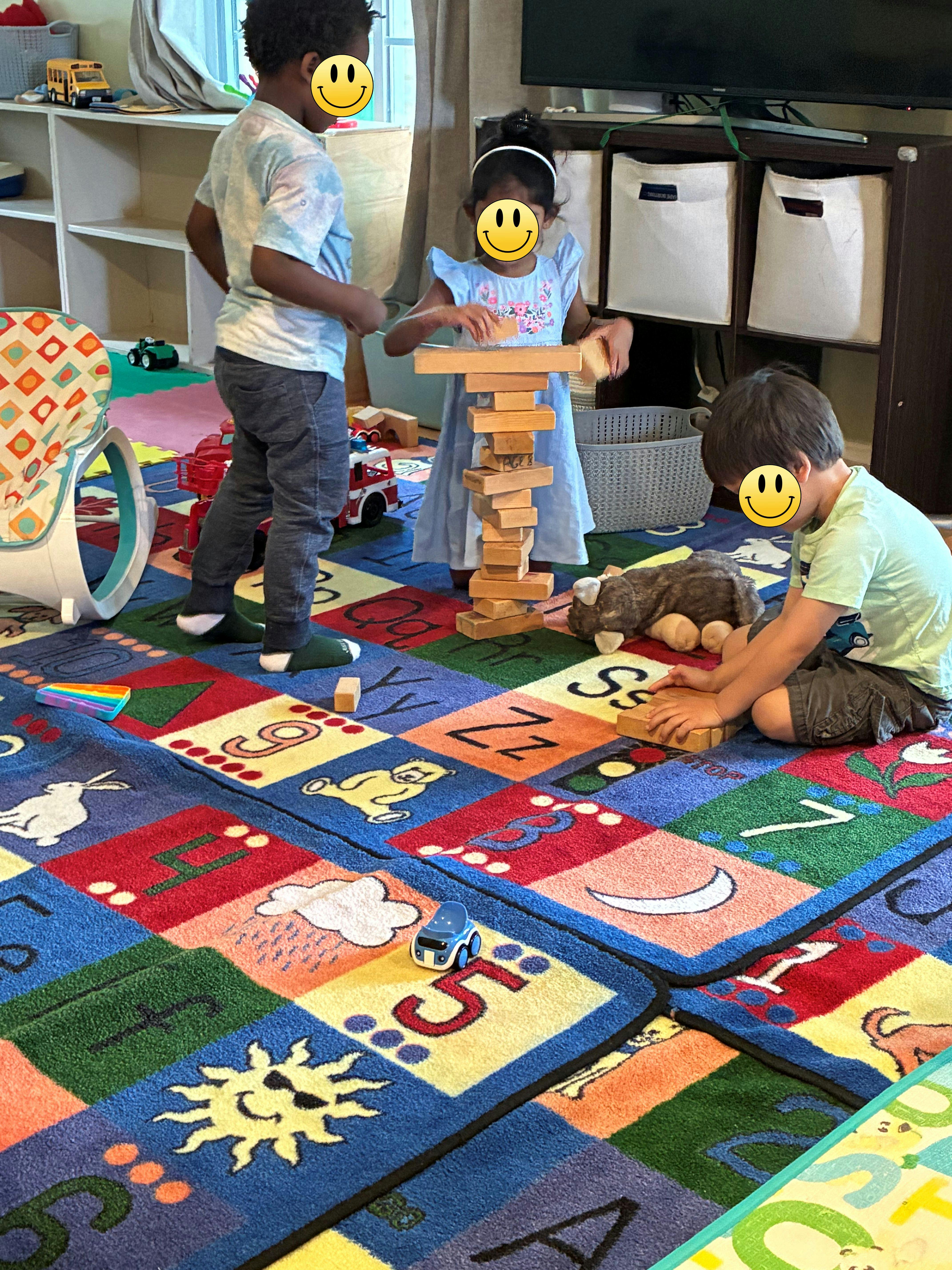 Three children playing with a wooden block tower on an alphabet rug