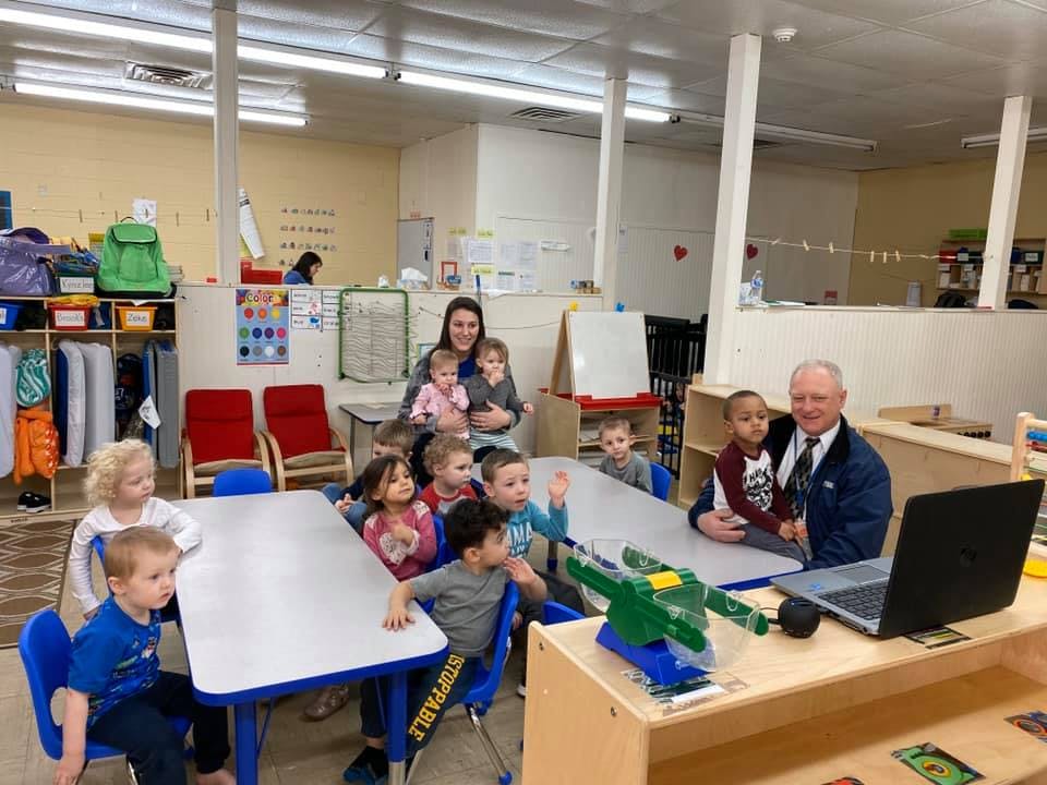 Adults and children gathered around tables in a classroom
