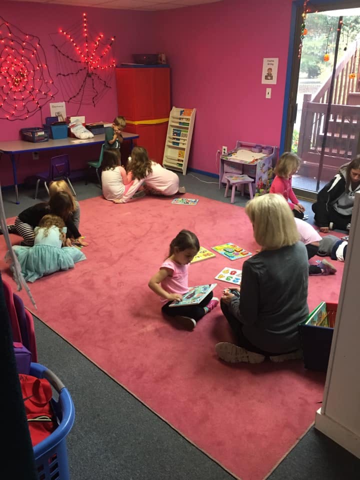 Adult and children sitting on a rug, some reading books