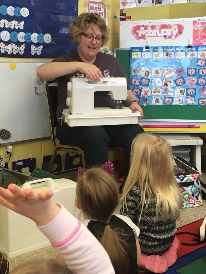 Person demonstrating a sewing machine to children in a classroom