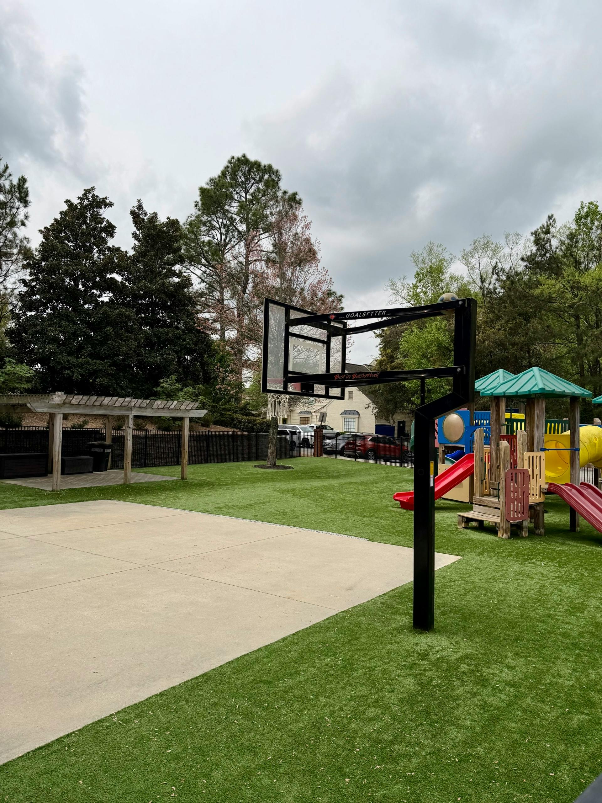 Basketball hoop on a playground with a concrete court and play structure