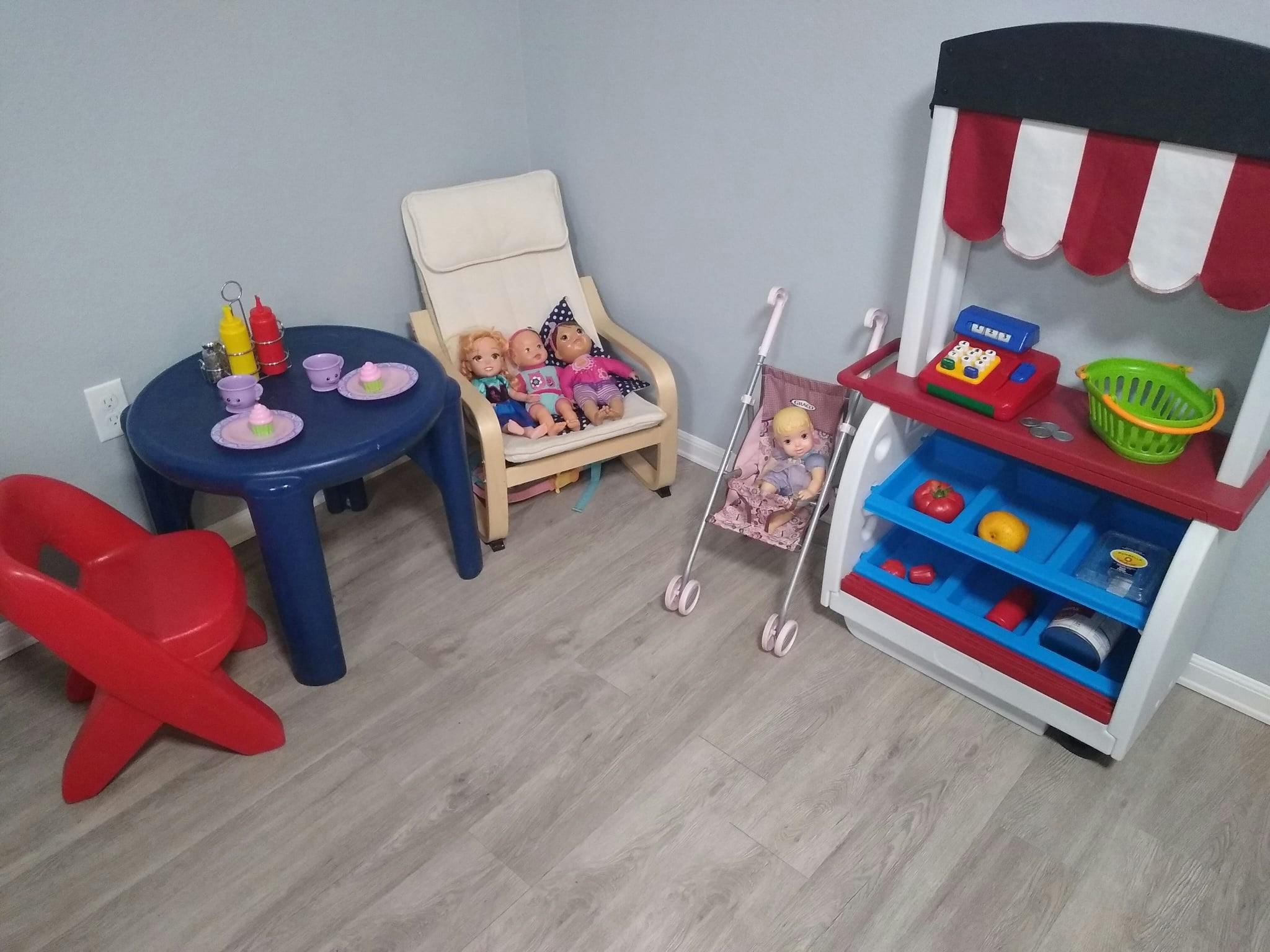 Playroom with toy table, chair with dolls, doll stroller, and toy market stand