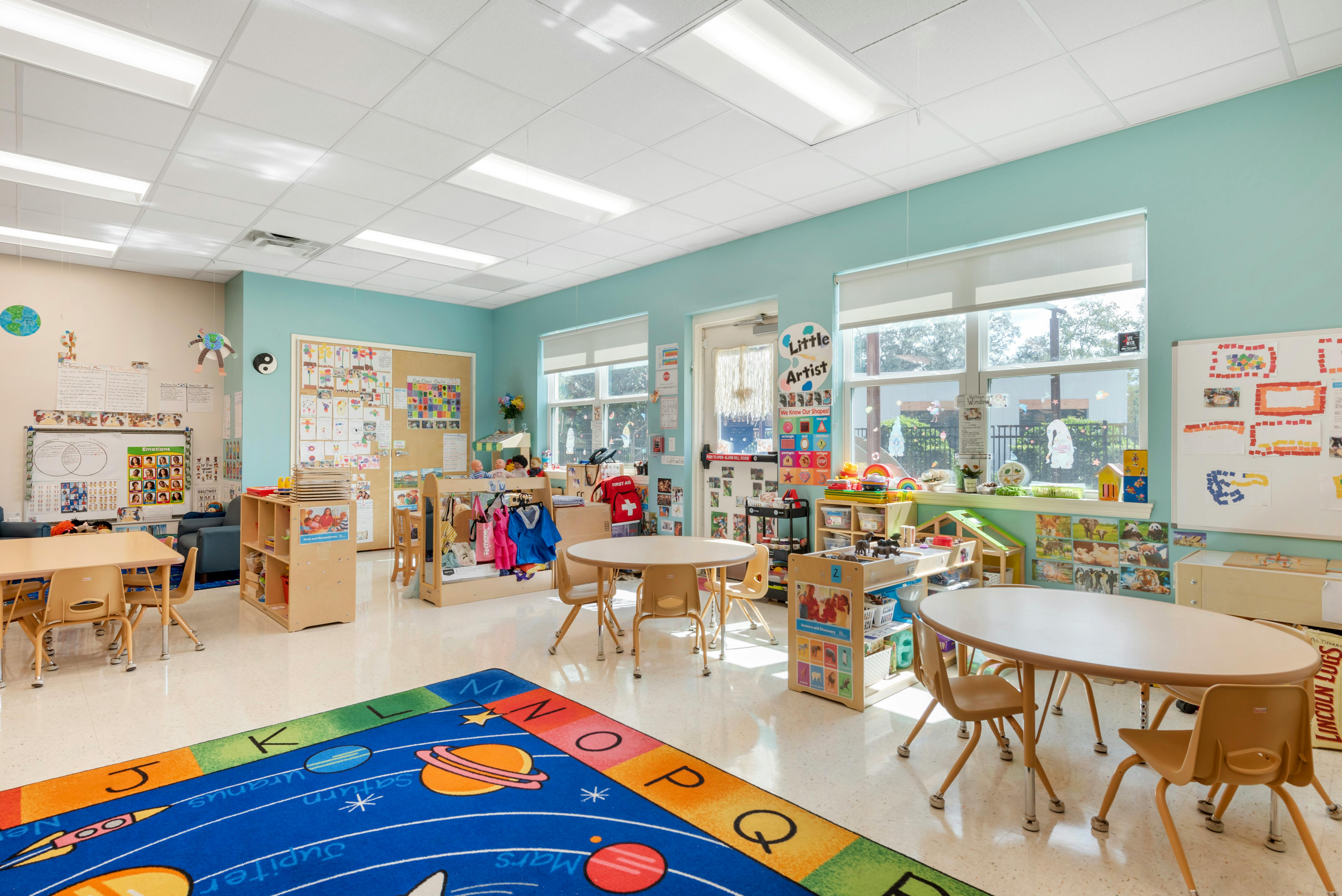Empty classroom with small tables and chairs, colorful rug