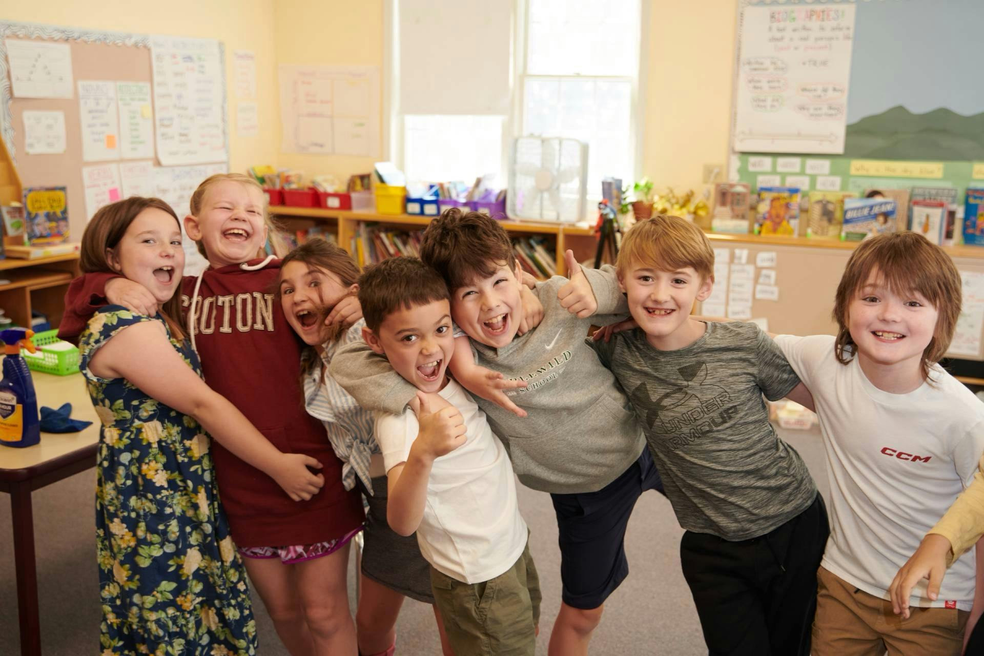 Seven children laughing with arms around each other in a classroom