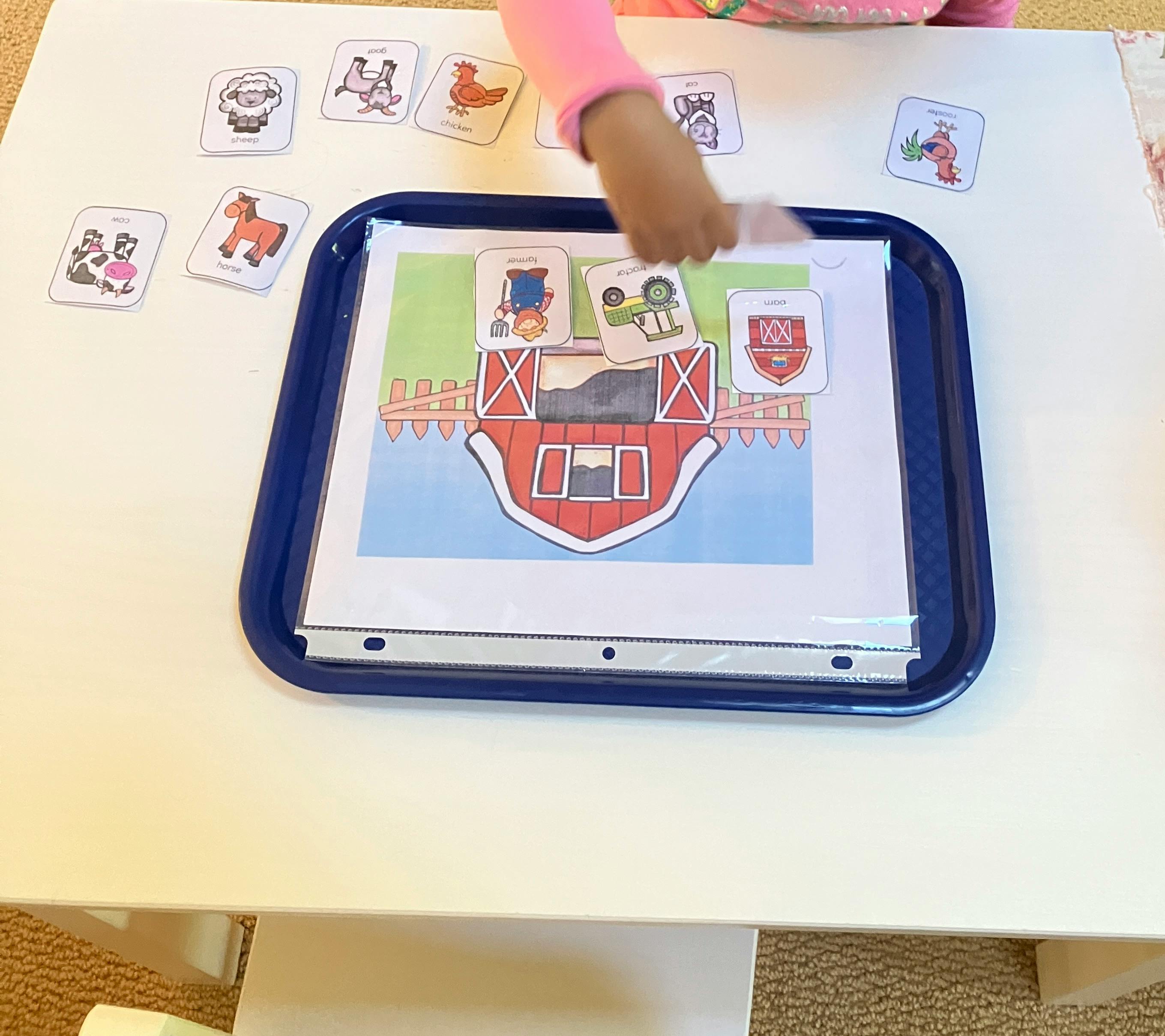 Child's hand placing a card on a farm-themed activity mat