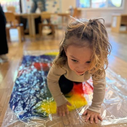 Child playing with colorful paint in a plastic bag on the floor