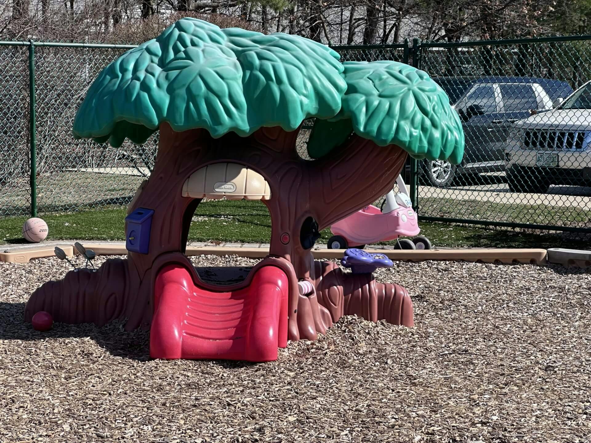 Plastic play structure shaped like a tree with a red slide