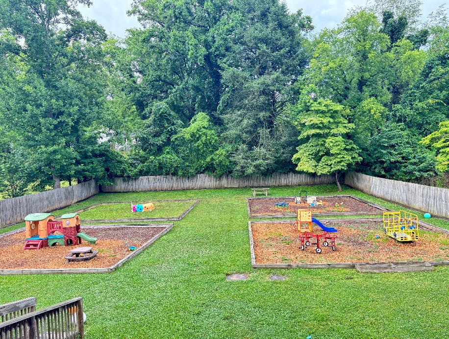 Playground equipment in a grass yard surrounded by a wooden fence