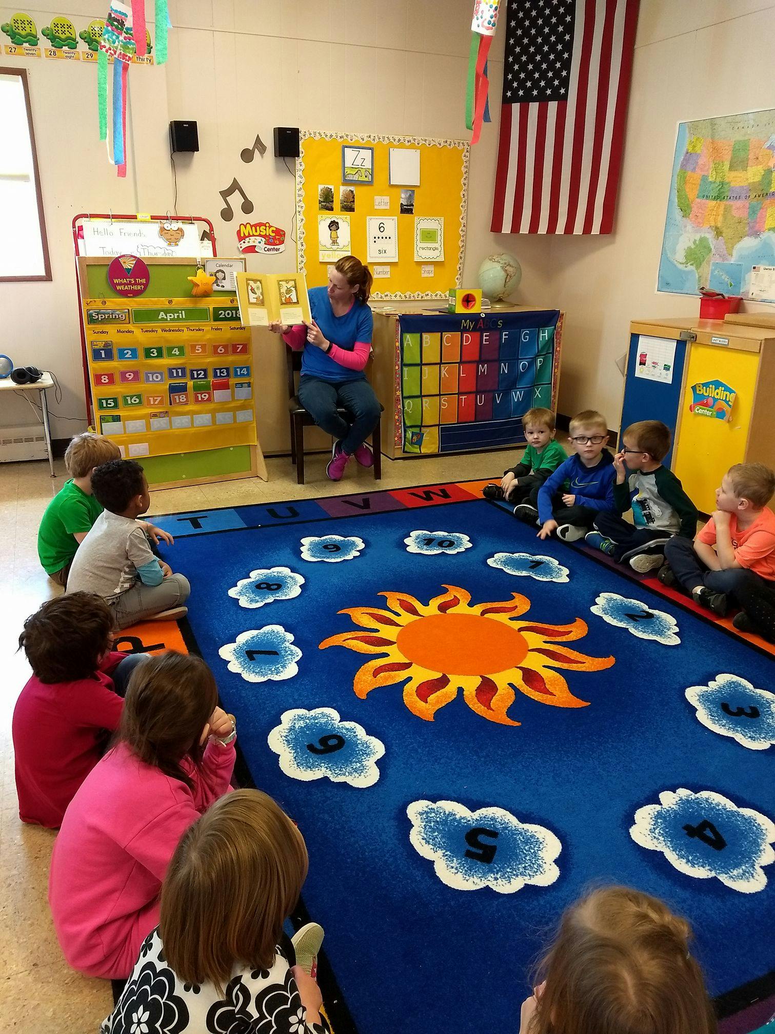 Adult reading a book to children sitting on a rug in a classroom