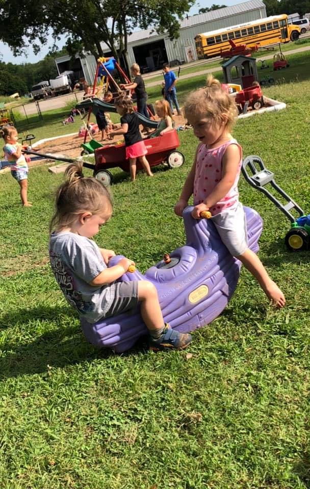 Two children playing on a purple seesaw in a grassy area