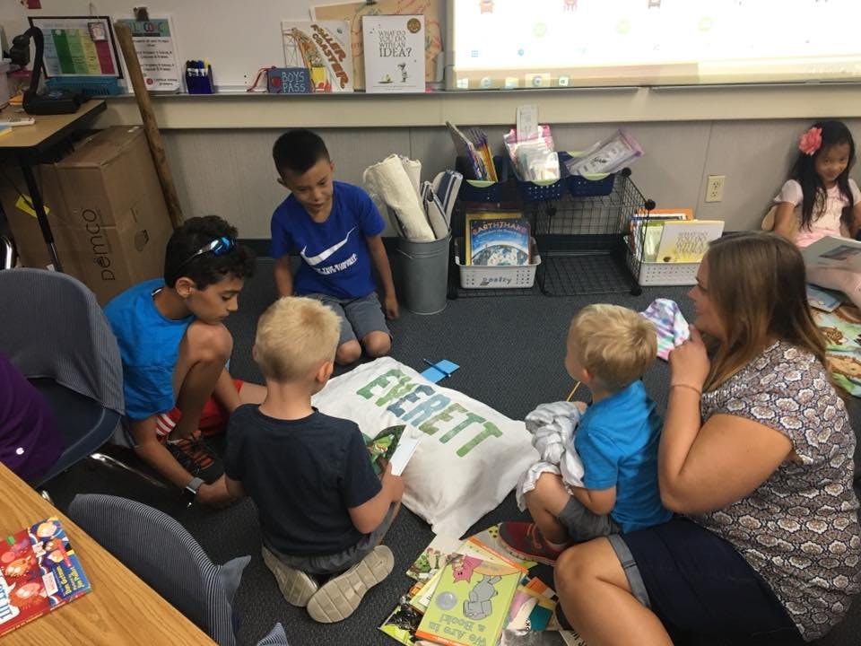 Adult and children sitting on floor looking at a pillow with "EVERETT" on it