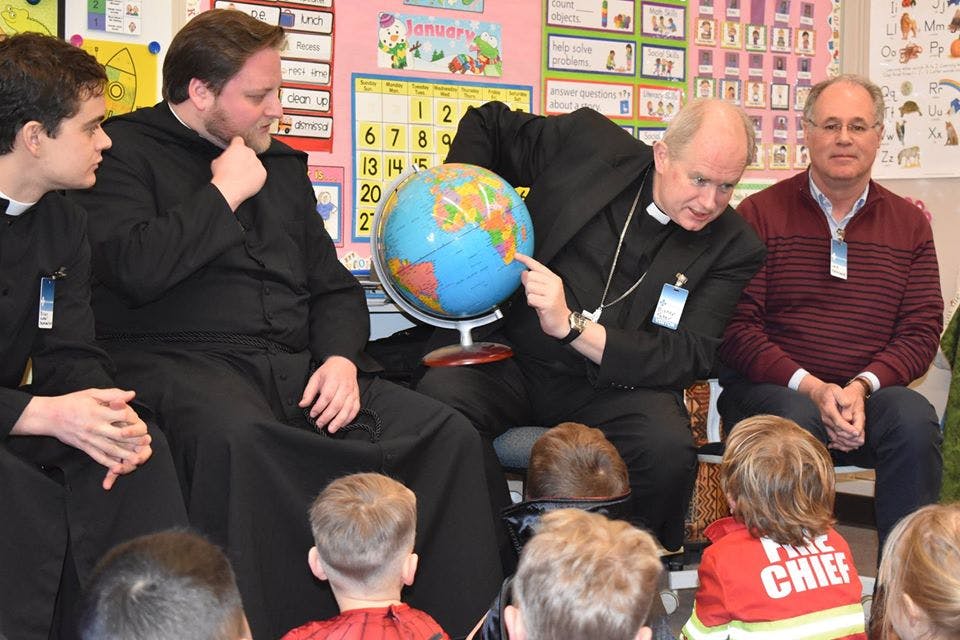 Adults and children gathered around a globe in a classroom
